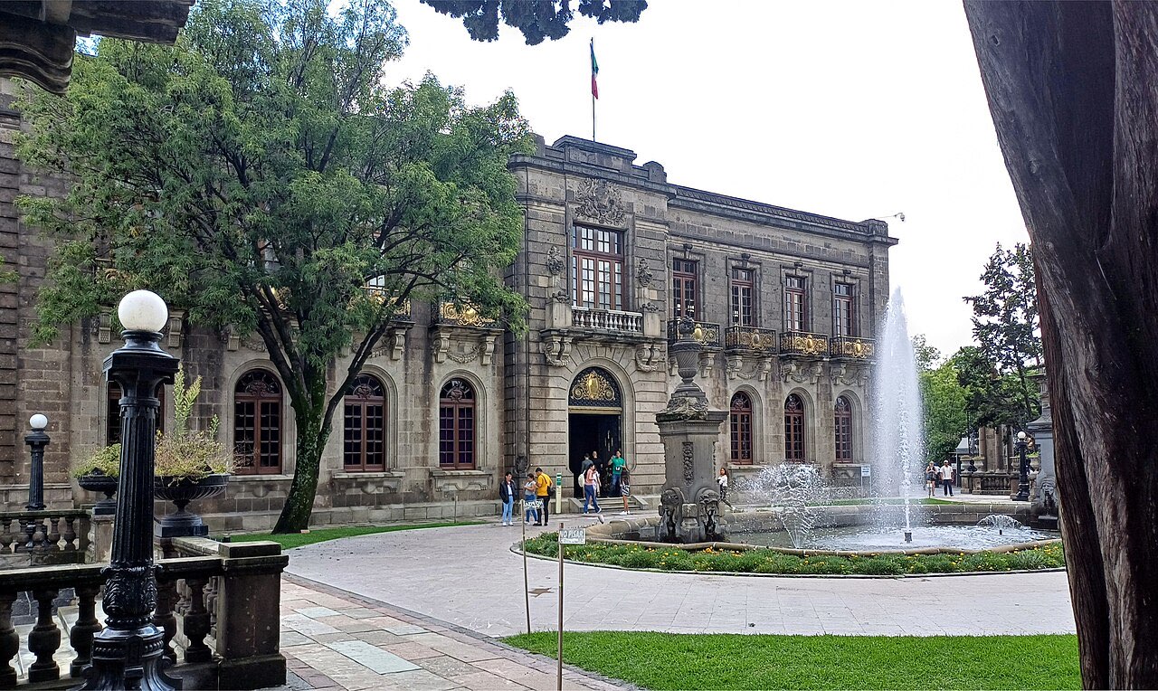 Stone facade of Chapultepec Castle with a fountain and trees in the foreground
