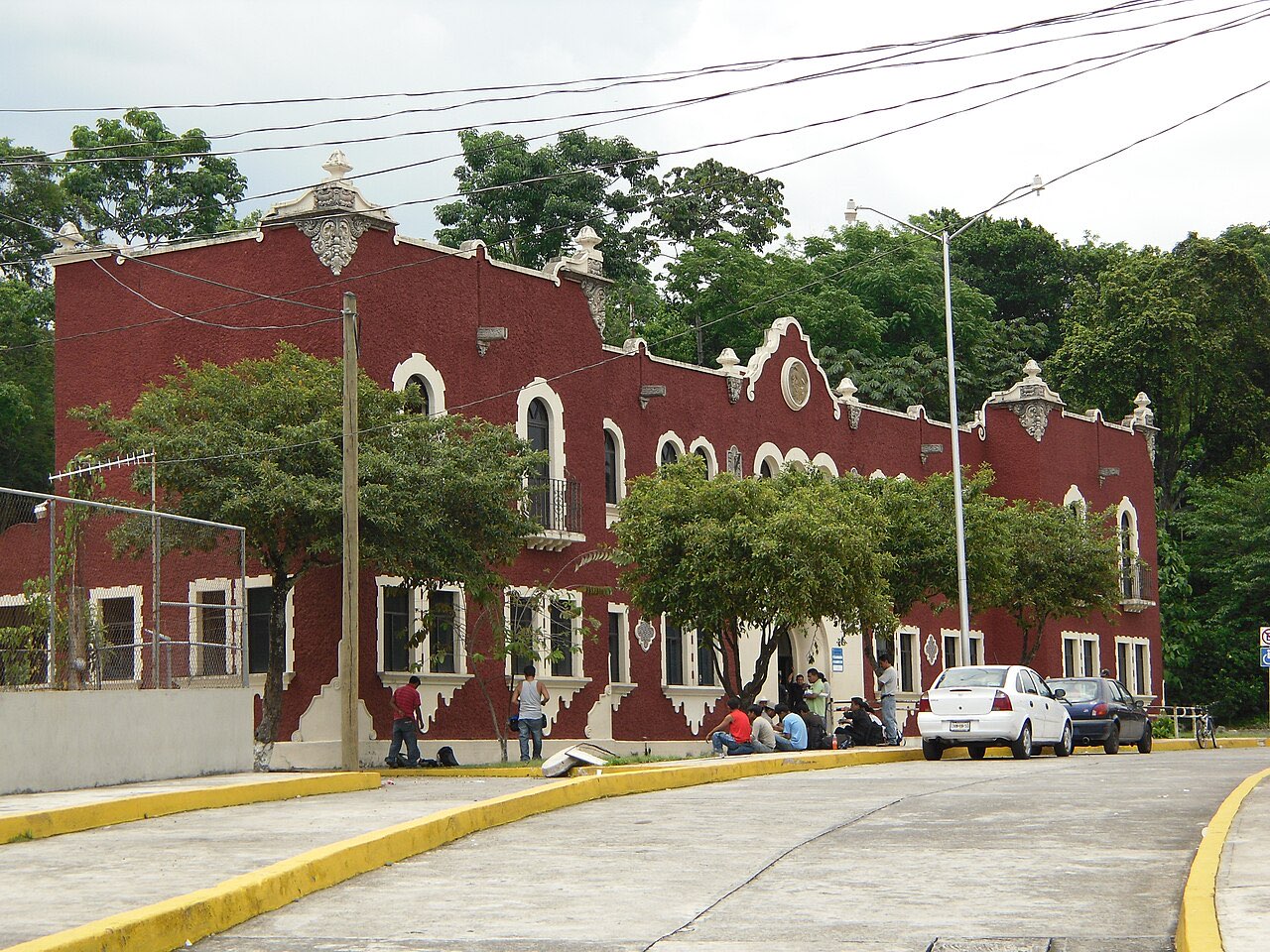 A red two-storey building with cream trim housing a Mexican Instituto Nacional de Migración office, with cars parked outside