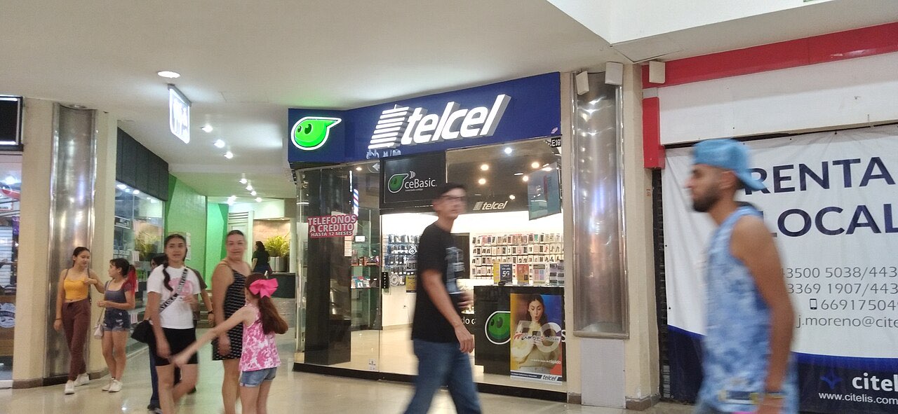 Storefront of a Telcel shop inside a shopping mall, with a lit blue Telcel sign above the entrance