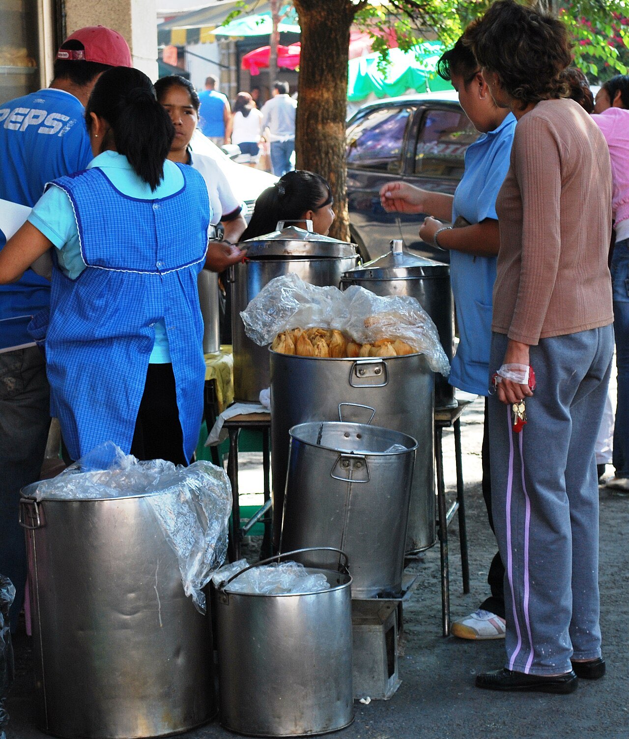 Vendors serving tamales from large steel pots at a street stand in Mexico City