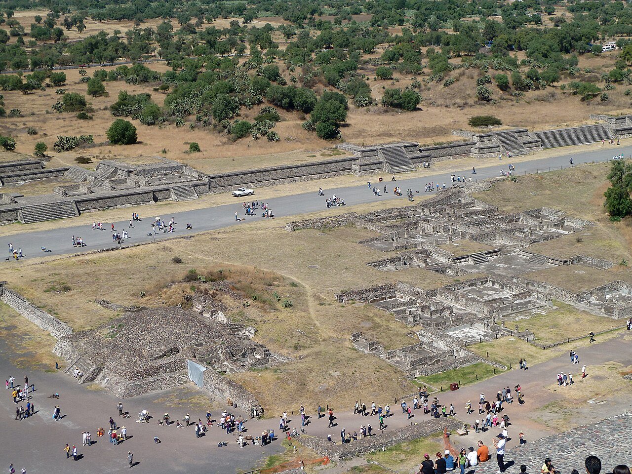 Aerial-style view from the top of a pyramid down onto ruined temple compounds, the Avenue of the Dead and small groups of visitors